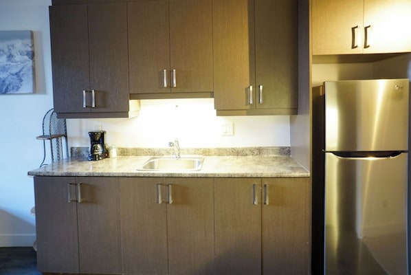 A kitchen with a stainless steel refrigerator, a coffee maker, and a sink.