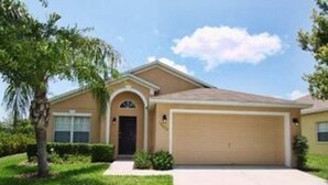 A single-story house with a beige facade, a dark brown garage door, and a small front yard with a palm tree and shrubs. - Lakeside in Clermont (Clermont)