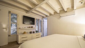 A bedroom with a bed, a TV mounted on the wall, a dresser, and a door with blinds. - Santos de Piedra Exclusive Home (Provincia de Cartagena)