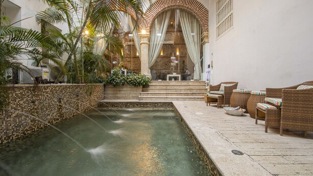A pool area with a fountain, wicker furniture, and a view of a building with arches and a balcony. - Santos de Piedra Exclusive Home (Provincia de Cartagena)