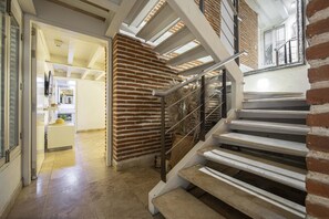 Un escalier avec une rampe en métal, des murs en briques et une vue sur un espace cuisine.