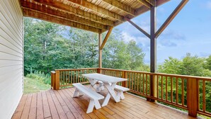Una terraza de madera con una mesa de picnic y bancos, con vista a un área boscosa.