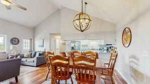 Un salón amplio con zona de comedor, sillas de madera, una lámpara de araña y una cocina al fondo.