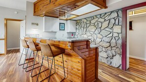 Una cocina con pared de piedra, vigas de madera en el techo y una barra con taburetes.