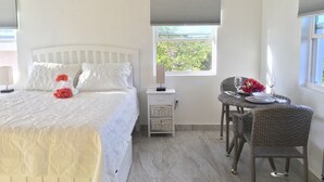 Un dormitorio con cama, mesita de noche, una silla de mimbre y ventana con vistas.