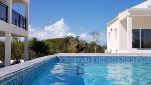 Una piscina con agua cristalina azul, rodeada de edificios blancos y vegetación.