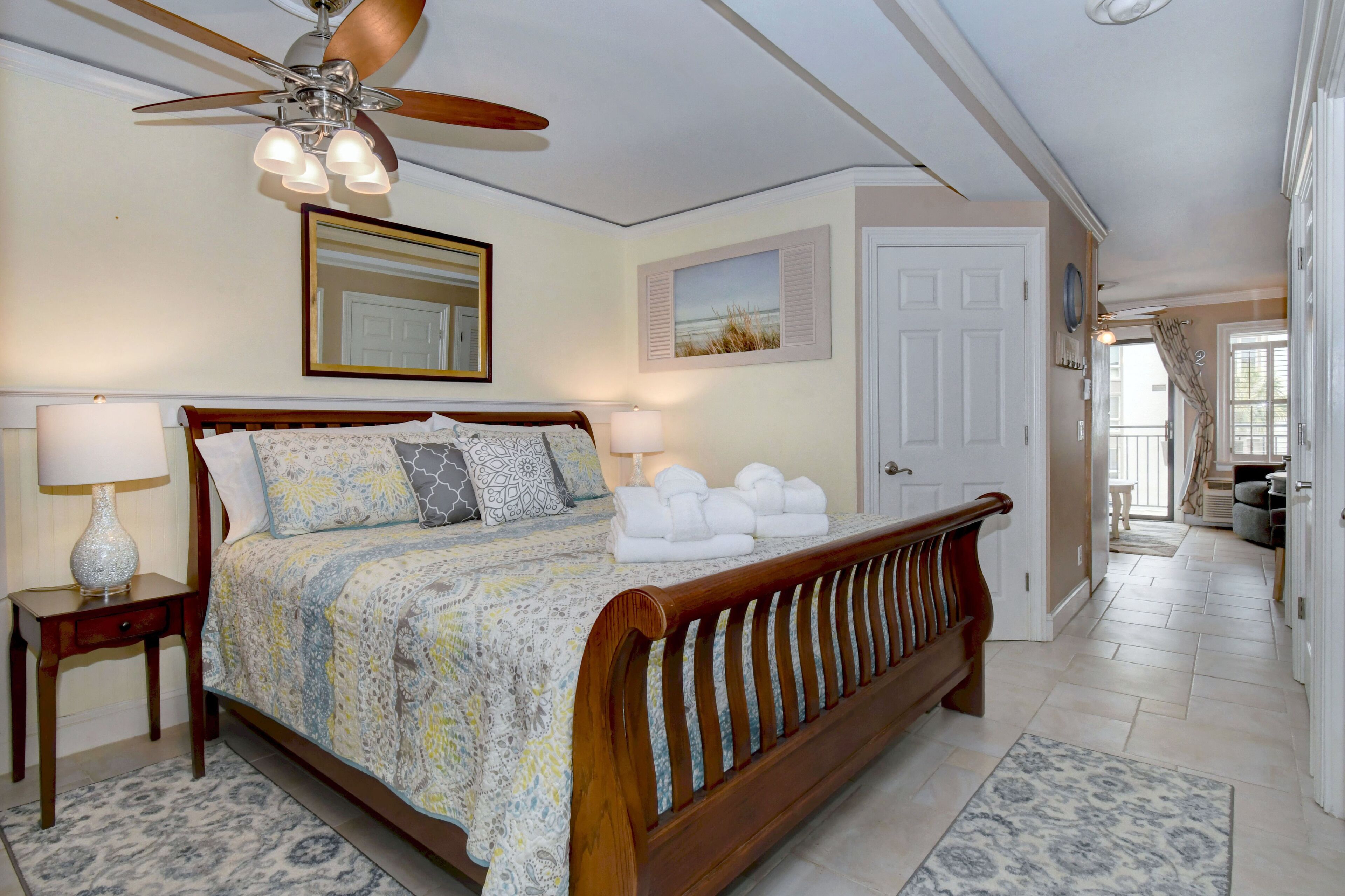A bedroom with a wooden bed, a ceiling fan, and a view of the hallway.
