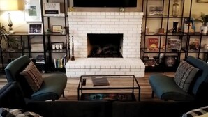 Ein Wohnzimmer mit Kamin aus weißen Ziegelsteinen, einem flachbildfernseher darüber montiert und zwei Sesseln mit einem Couchtisch in der Mitte.