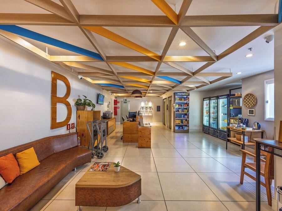 Un hall espacioso con mostrador de recepción, zona de estar, máquinas expendedoras y un gran letrero con la letra 'B' en la pared.