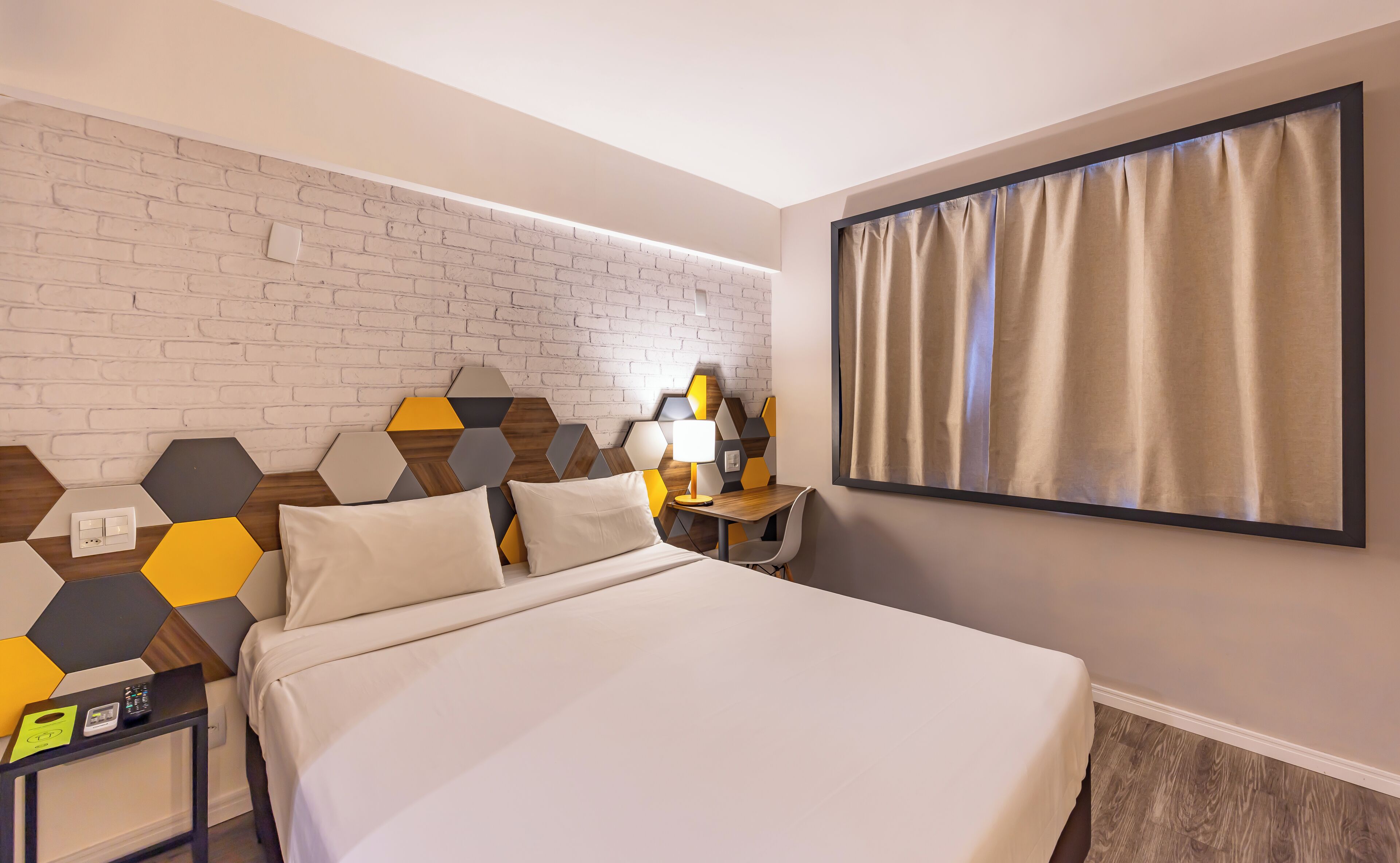 A hotel room with a bed, a nightstand, a lamp, and a wall with a geometric pattern.
