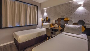 A hotel room with two beds, a desk, a chair, a window with curtains, and a brick-patterned wall. - B&B Hotels Rio de Janeiro Norte (Rio de Janeiro)