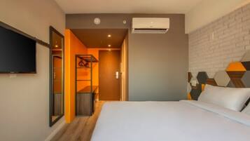 Quarto de hotel com cama, ar condicionado, televisão e cabeceira com padrão de tijolos.