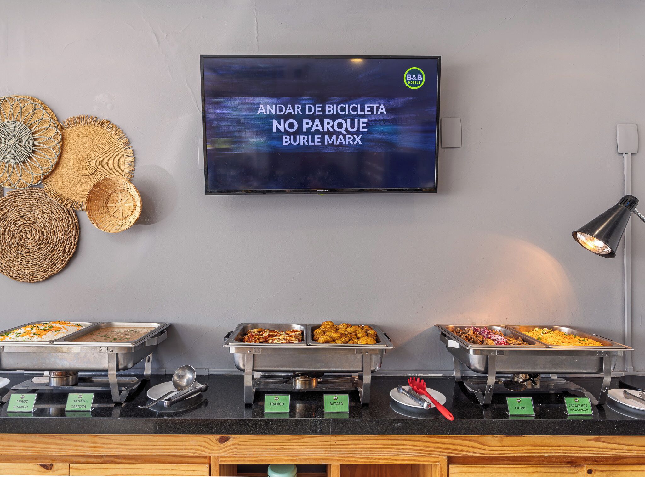 Un área de bufé con opciones de comida señalizadas, un televisor mostrando un mensaje y cestas tejidas en la pared.