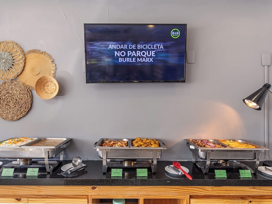 A buffet area with labeled food options, a television displaying a message, and woven baskets on the wall.