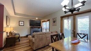 A cozy living room with a fireplace, a television, and a dining area with a table and chairs. - Charming Fire Mountain Lodge Condo | Walk to Downtown | Sleeps Six  (Canmore)