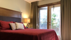 A hotel room with a large bed, a nightstand with a lamp, and a view through a glass door. - Charming Fire Mountain Lodge Condo | Walk to Downtown | Sleeps Six  (Canmore)