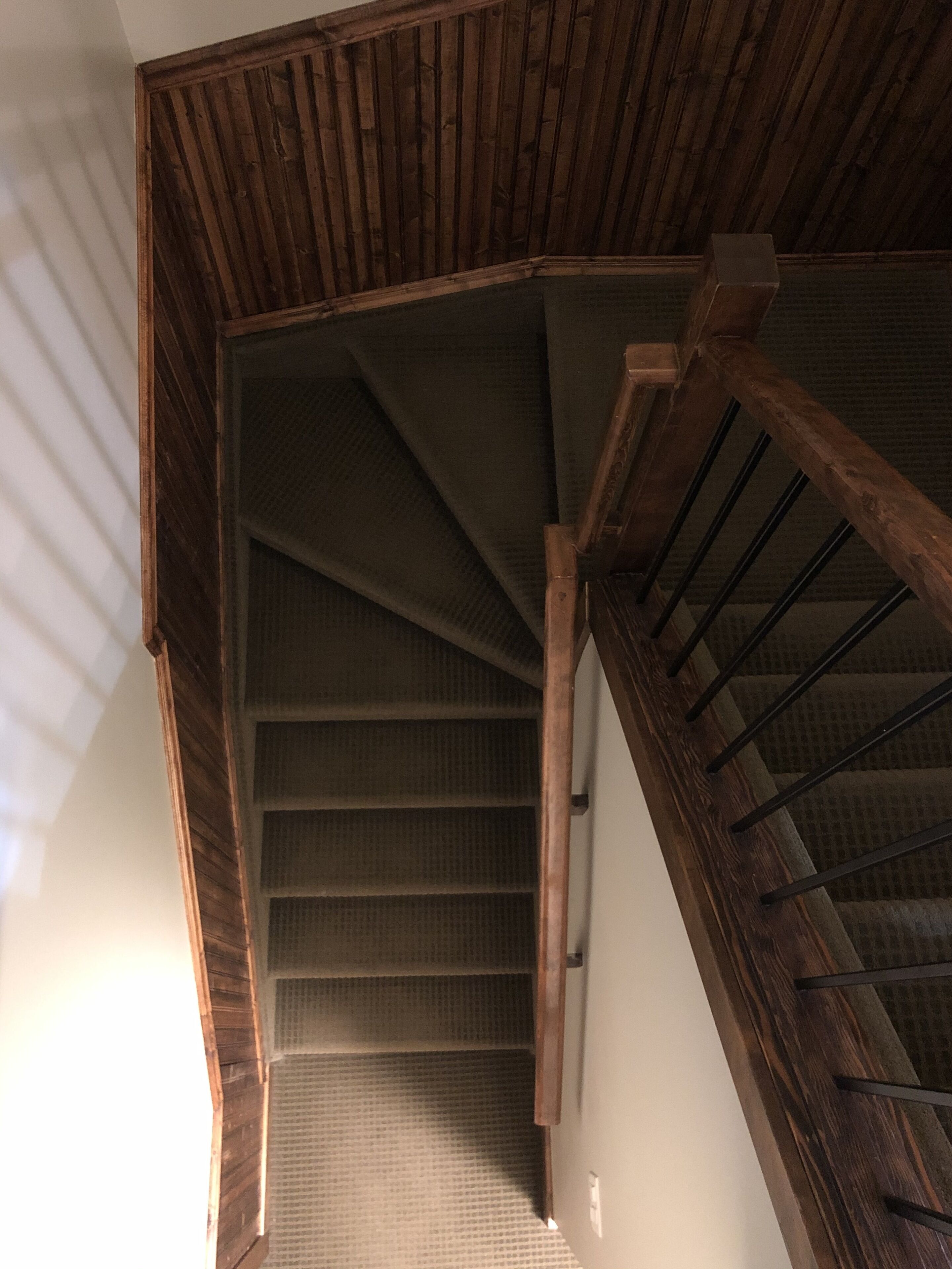 A wooden staircase with a textured carpet, leading to a lower level.