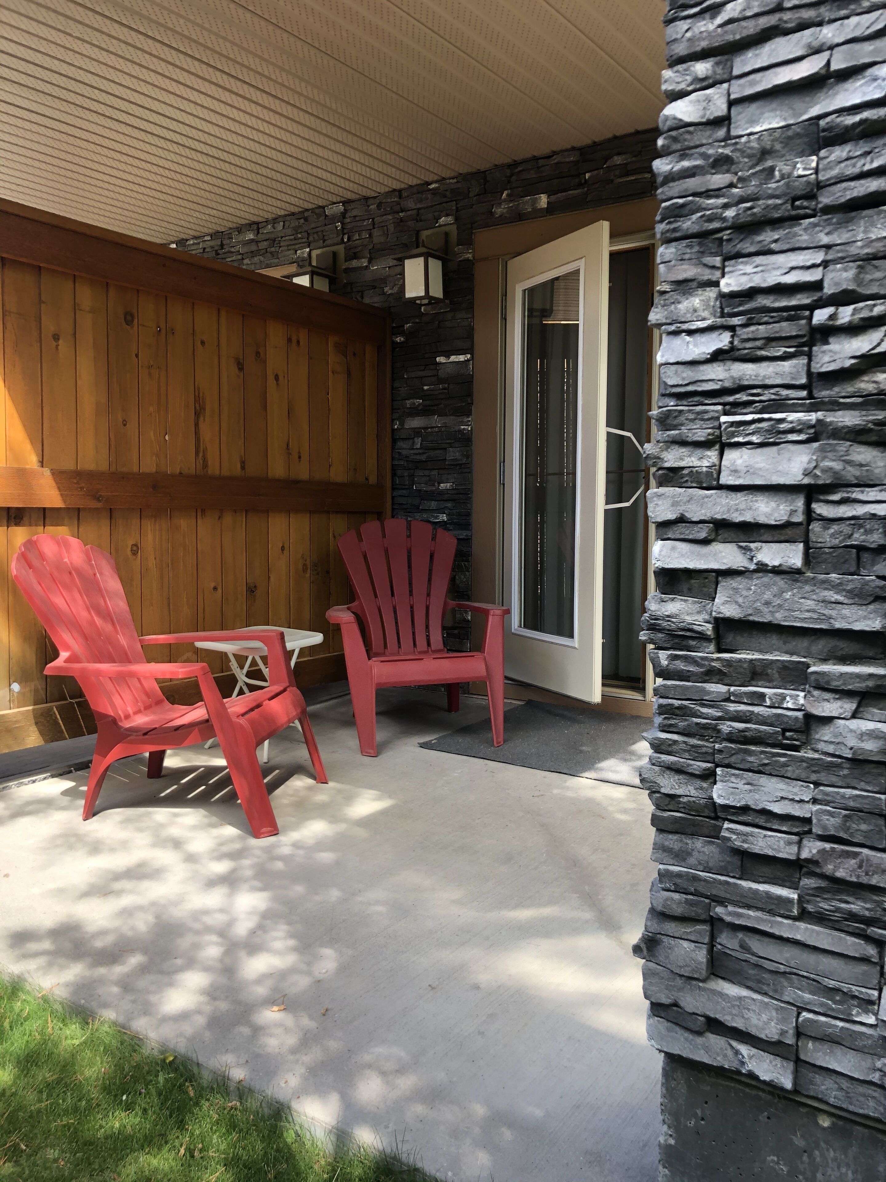 Un patio con dos sillas Adirondack rojas, una valla de madera y un muro de piedra.
