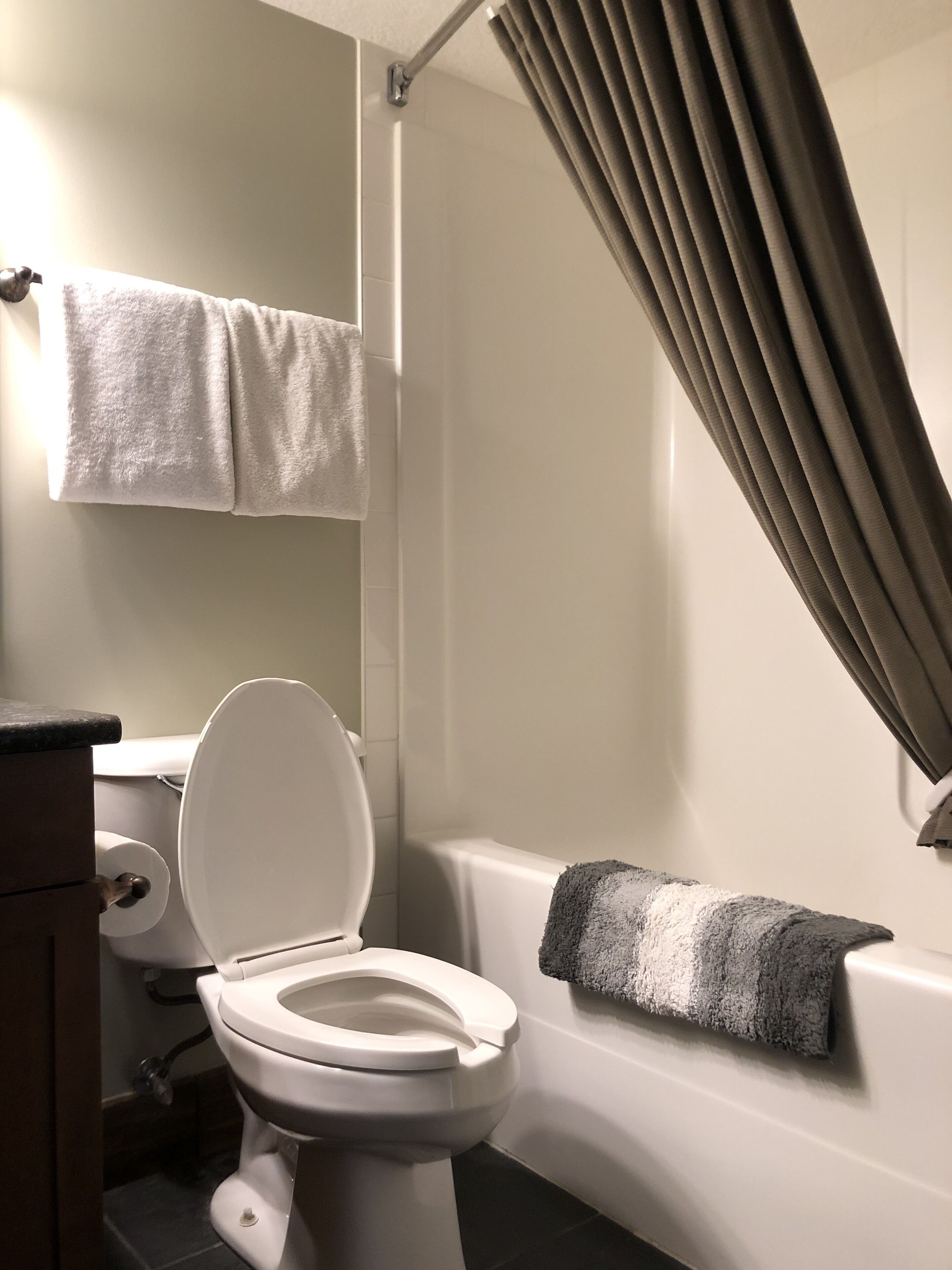 Une salle de bain avec des toilettes, une baignoire, un rideau de douche et une serviette accrochée au mur.