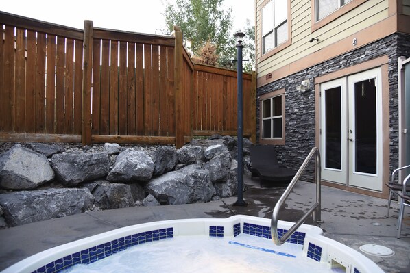 A hot tub area with a wooden fence, stone wall, and a building with stone and wood siding. - Charming Fire Mountain Lodge Condo | Walk to Downtown | Sleeps Six (Canmore)