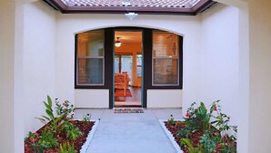 A house entrance with a tiled roof, a door with a glass panel, and a pathway leading to a room with a chair and a table. - Brand New Home Close to Sequoia /w Tub & Games (Visalia)