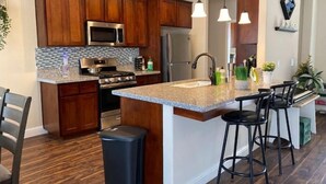 A kitchen with wooden cabinets, stainless steel appliances, a granite countertop, and a bar area with stools. - Brand New Home Close to Sequoia /w Tub & Games (Visalia)