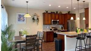 A modern kitchen with wooden cabinets, stainless steel appliances, and a central island with bar stools. - Brand New Home Close to Sequoia /w Tub & Games (Visalia)