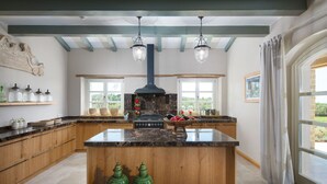 A spacious kitchen with a large island, wooden cabinets, and a black stove. There are two hanging lights and a window with a view of greenery. - Villa Terra Verde with Pool (Kanfanar)