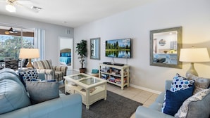 A modern living room with a sofa, armchair, coffee table, and TV. There is a bookshelf and a plant. - Gorgeous Davenport 5 Bed Villa With Pool Hot Tub (Davenport)