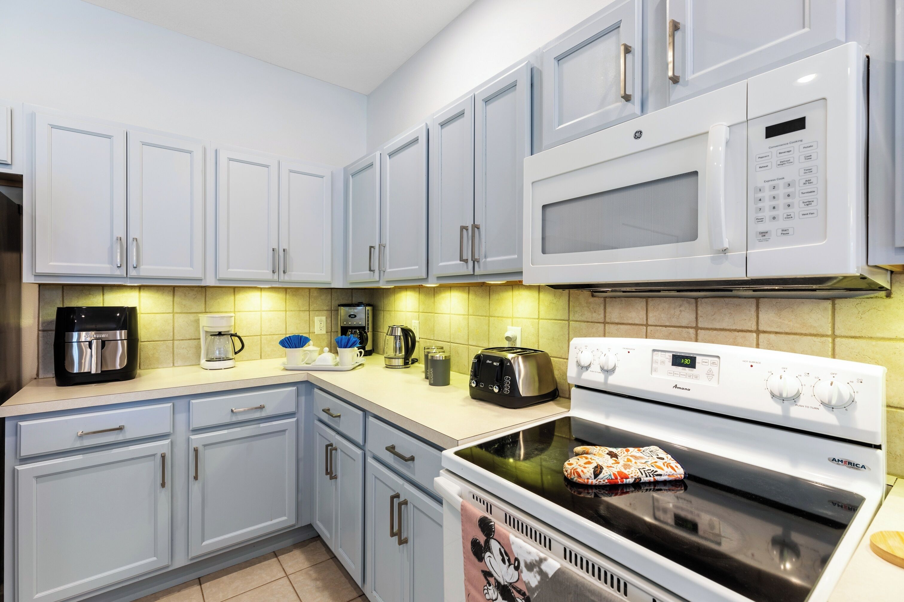 Une cuisine avec des meubles de couleur bleu clair, un four à micro-ondes blanc, une cuisinière et un grille-pain.