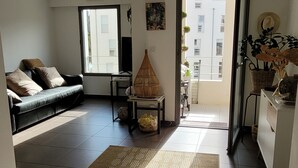 Una sala de estar con un sofá, una mesita, una planta decorativa y vistas al balcón exterior.