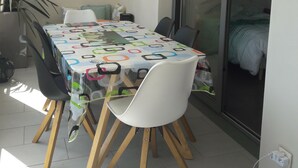 Un comedor con una mesa cubierta por un mantel colorido, rodeado de sillas blancas.