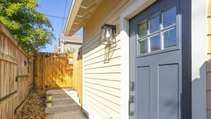 Un étroit sentier mène à une maison bordée d’une clôture en bois d’un côté et d’une porte de garage blanche de l’autre.