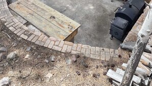 En uteplats med ett träbord och stolar, en grill och en mur av tegelsten.