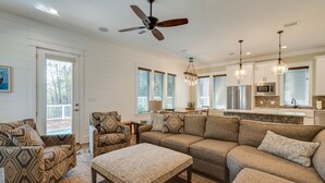 A spacious living room with a sectional sofa, a coffee table, and patterned armchairs. There is a ceiling fan, pendant lighting, and a kitchen area visible in the background. - Sea Glass Cottage ~ Private Pool ~ Private Beach Access ~ Golf Cart Included! (Miramar Beach)