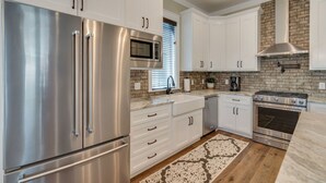 A modern kitchen with stainless steel appliances, white cabinetry, and a brick backsplash. - Sea Glass Cottage ~ Private Pool ~ Private Beach Access ~ Golf Cart Included! (Miramar Beach)