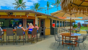 An outdoor restaurant with tables and chairs, palm trees, and a clear blue sky. - Stunning ocean views & direct beach access (Lahaina)