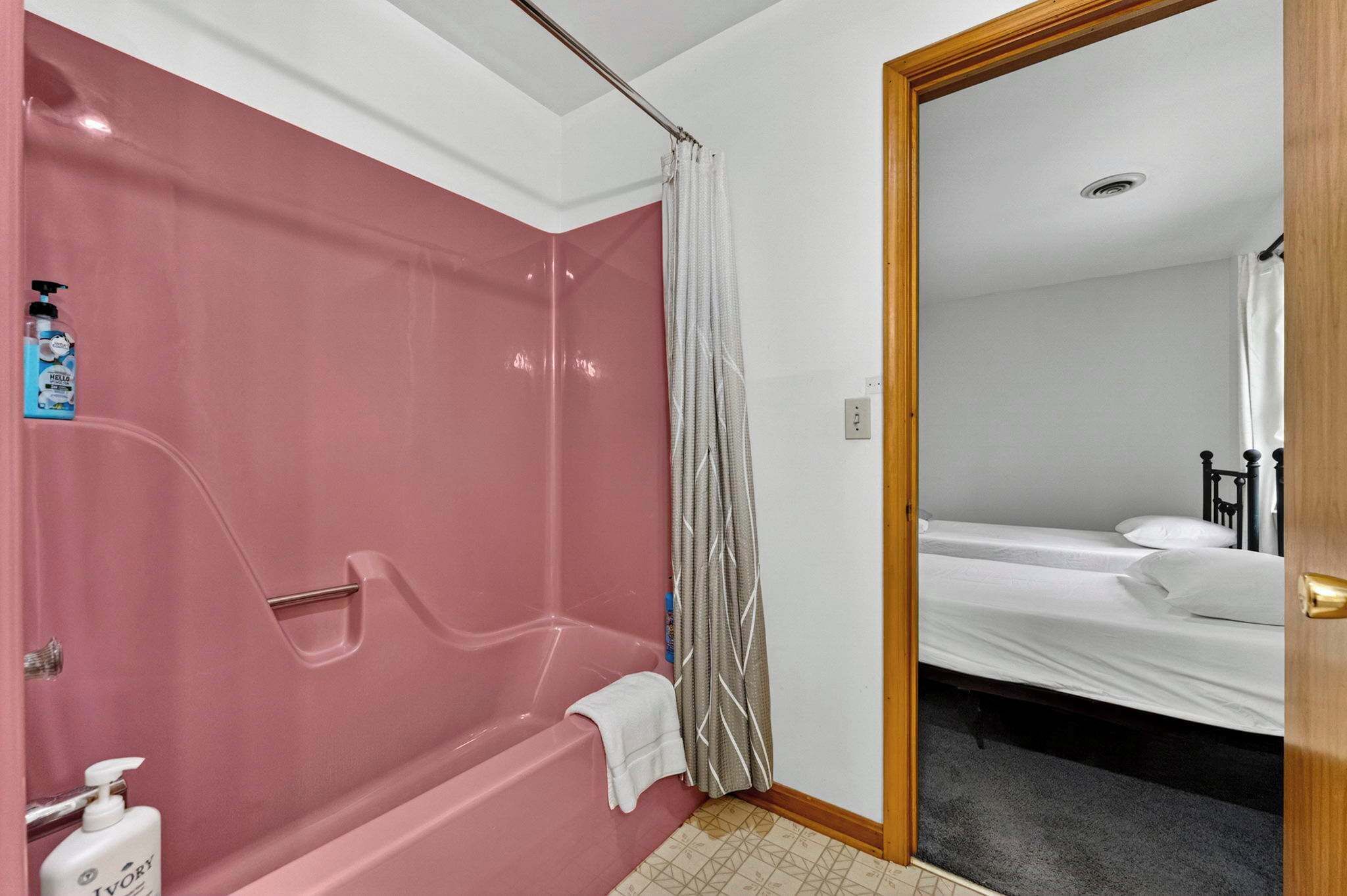 Ein Badezimmer mit einer rosa Badewanne, einer Duschvorhangs und einem weißen Handtuch auf dem Boden.