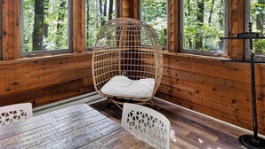 A wooden cabin interior with a wicker chair, a table, and a standing lamp. - Huge Cabin w Hot Tub, Deck, Grill & WiFi (Berkeley Springs)