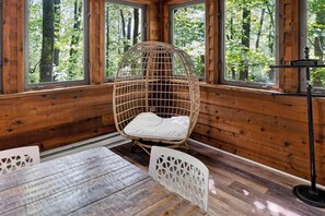 A wooden cabin interior with a wicker chair, a table, and a standing lamp.
