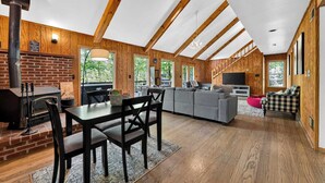 A spacious living area with a fireplace, wooden beams, a sofa, and a television. - Huge Cabin w Hot Tub, Deck, Grill & WiFi (Berkeley Springs)