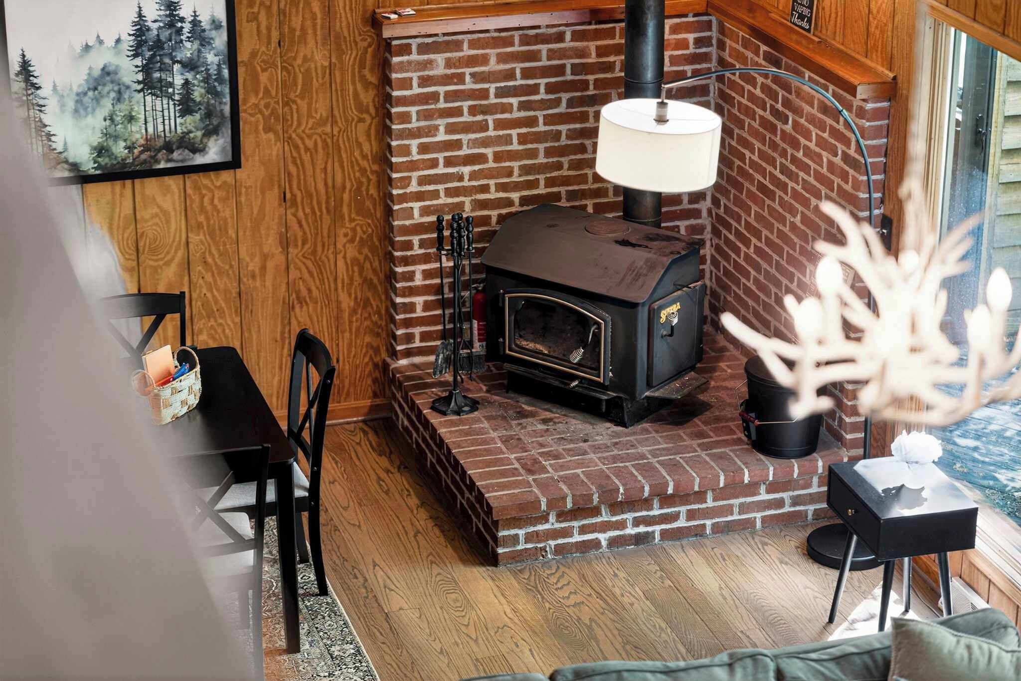 A cozy room with a brick fireplace, a table with chairs, and a window with a view of trees.