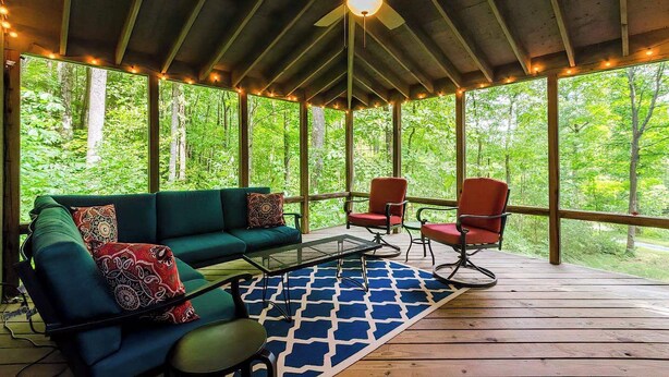 A covered outdoor seating area with a green sofa, red chairs, and a ceiling fan. - Secluded Oasis w Hot Tub, Screened-in Porch, WiFi! (Berkeley Springs)