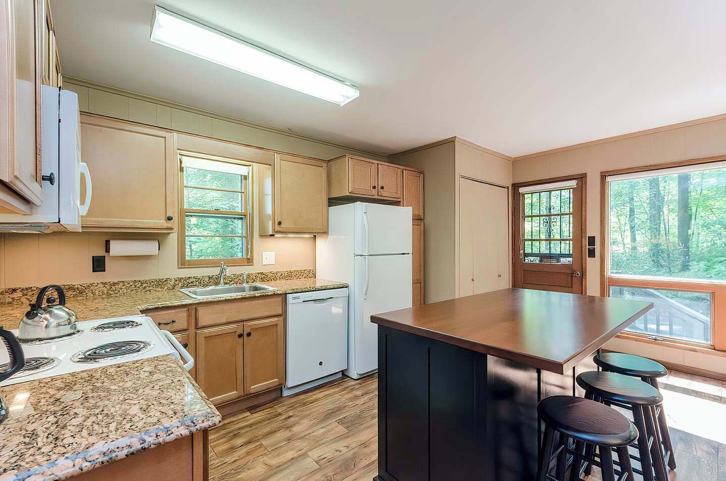 A compact kitchen with wooden cabinets, a granite countertop, a built-in stove, a refrigerator, and a bar area with stools.