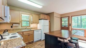 A compact kitchen with wooden cabinets, a granite countertop, a built-in stove, a refrigerator, and a bar area with stools.