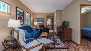 A compact living room with a blue sofa, a wooden coffee table, a television, and a patterned rug. - Secluded Oasis w Hot Tub, Screened-in Porch, WiFi! (Berkeley Springs)
