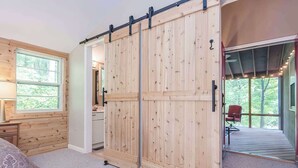 A bedroom with a large sliding door, a bed, a nightstand, a dresser, and a window with a view of the outdoors. - Secluded Oasis w Hot Tub, Screened-in Porch, WiFi! (Berkeley Springs)