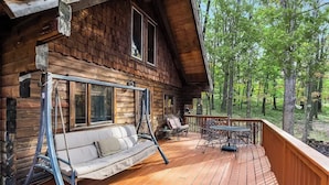 A wooden cabin with a swing chair, a sofa, and a dining table on the deck.