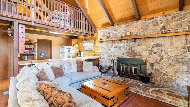 A cozy living room with a stone fireplace, a wooden ceiling, and a loft area with a balcony.