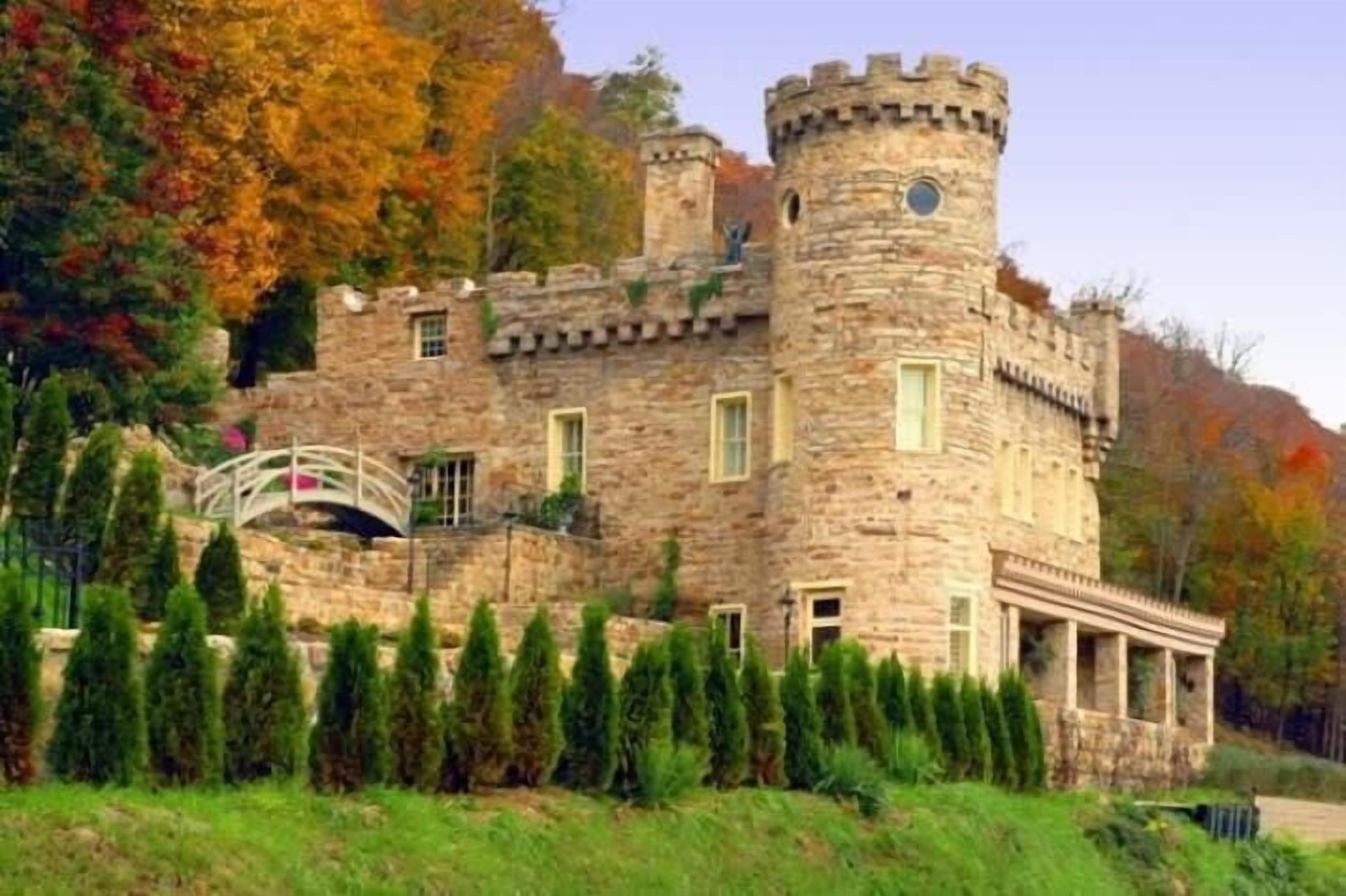 Un edificio de estilo castillo con una torre, un puente y un césped cuidado.